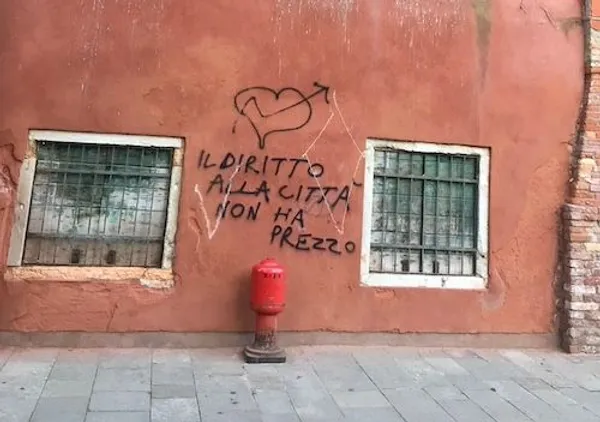 Graffiti against a red wall with a writing reading "il diritto alla città non ha prezzo", in Venice, Italy